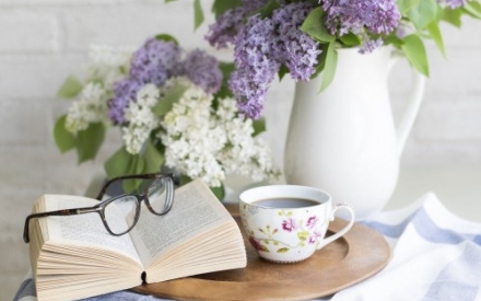 Ein Tisch mit Blumen, einem aufgeschlagenen Buch und einer Tasse Kaffe.