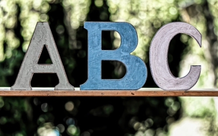 Die drei Buchstaben ABC, gefertigt aus buntem Karton stehen auf einem Brett.