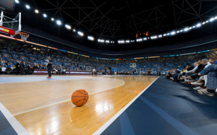 Ein Basketball-Spielfeld aus Weitwinkelperspektive. Die Spielfl&auml;che ist leer, im Vordergrund liegt ein Basketball auf dem Boden.