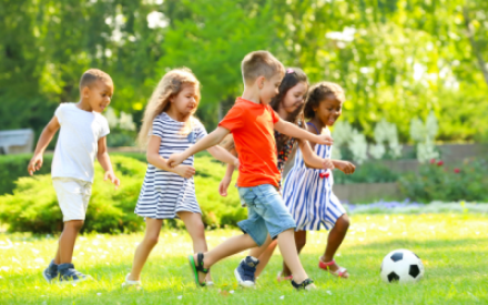 Auf einer leuchtend gr&uuml;nen Wiese spielen Jungen und M&auml;dchen gemeinsam Fu&szlig;ball. Sie lachen und rennen.