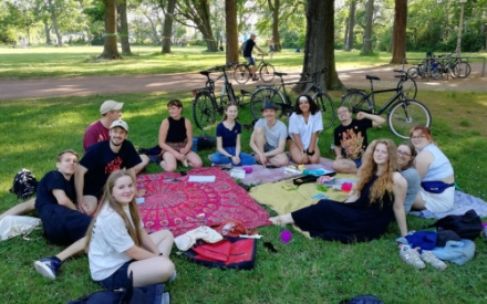 junge Menschen sitzen auf bunten Decken auf einer Wiese im Park unter einem Baum