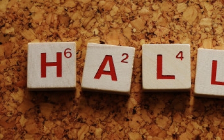 Auf einer Unterlage aus Kork liegt das Wort Hallo mit Scrabblebuchstaben