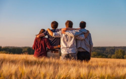 vier Jugendliche stehen in einem Getreidefeld vor blauem Himmel und legen sich gegenseitig die Arme auf die Schultern