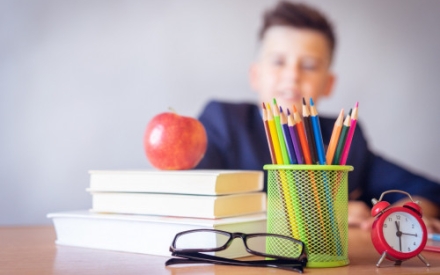 Junge am Schreibtisch, auf dem B&uuml;cher, Stifte und eine Brille liegen