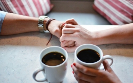 Zwei H&auml;nde die sich halten und Kaffetassen