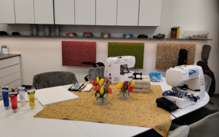 Auf einem TIsch liegen verschiedene Materialien und Tools f&uuml;r kreatives Tun: Farben, 2 N&auml;hmaschinen, Stoff, Papier und ein Tuschekasten