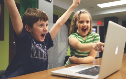 Zwei Kinder sitzen vor einem Computer und freuen sich.