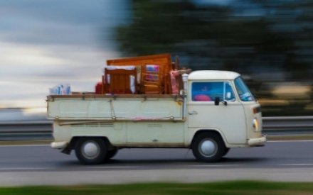 Auf einer Stra&szlig;e f&auml;hrt ein Pritschenwagen, der mit M&ouml;beln und Kram beladen ist. Der Hintergrund des Fotos ist verwischt und unscharf.