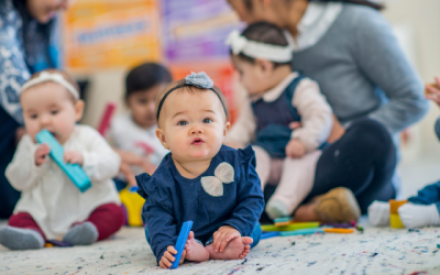 Auf einem Teppich sitzen mehrere kleine Kinder und Babies mit Spielzeug.