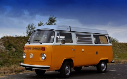 Ein alter VW-Bus in Orange steht auf einem Parkplatz.