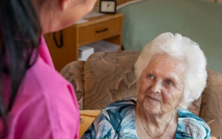 Eine Senior:innen sitzt und spricht mit einer jungen Frau.