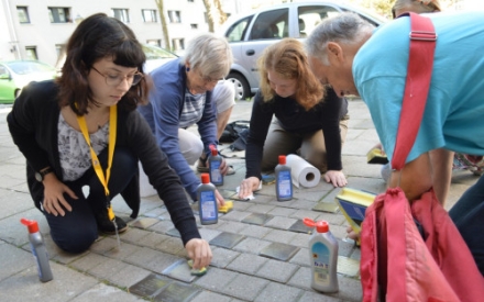 Eine Gruppe Menschen putzt gemeinsam Stolpersteine auf dem Gehweg.