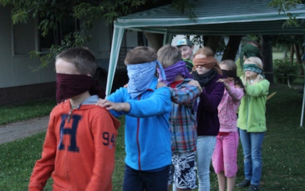 Mehrere Kinder stehen wie bei einer Polon&auml;se hintereinander und legen die H&auml;nde auf die Schultern der Person vor sich. Die Kinder haben die Augen verbunden.