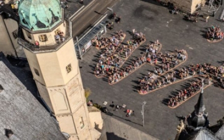 Das Logo des WIR-Festivals wird von Menschen auf dem Marktplatz von Halle nachgestellt. Auf dem Boden wurde ein riesiges WIR geschrieben, die Menschen haben sich so aufgestellt, dass die den Schriftzug nachbilden.