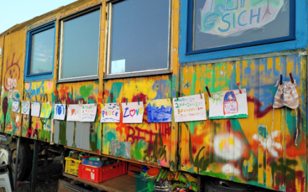 Ein bunt bemalter Bauwagen in Nahaufnahme, an dem ein Band h&auml;ngt mit vielen Kinderzeichnungen.