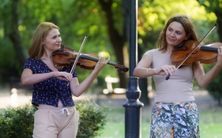 Zwei junge Frauen spielen im Park auf ihren Violinen.