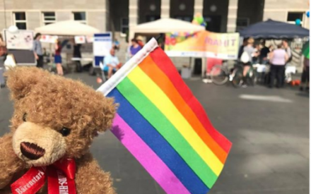 Der Aidshilfe-B&auml;r mit einer Regenbogenfahne. Im Hintergrund Infost&auml;nde auf dem Markplatz Halle.