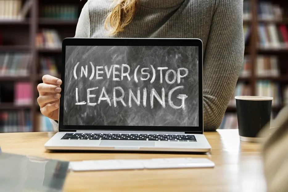 Ein Laptop auf einem Schreibtisch, auf dem Monitor steht "Never stop learning"