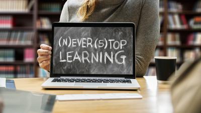 Ein Laptop auf einem Schreibtisch, auf dem Monitor steht "Never stop learning"