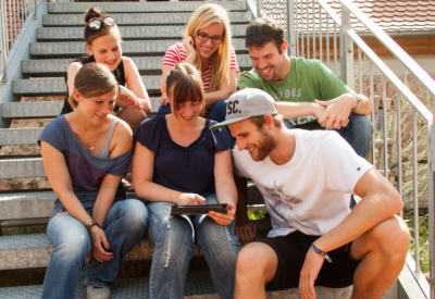 Jugendliche sitzen auf einer Treppe und schauen auf ein Tablet