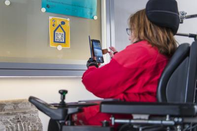 Eine Frau im Rollstuhl scannt einen QR-Code an einem Fenster