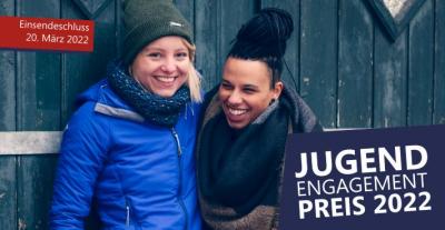 Zwei junge Menschen vor einer Holzwand | Text "Jugendengagementpreis 2022"