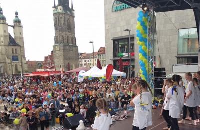 Zu sehen ist eine vor einer Bühne stehende Menschenmenge. Auf der Bühne tanzen Kinder. 