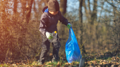 ein Junge steht in der Natur und sammelt Müll