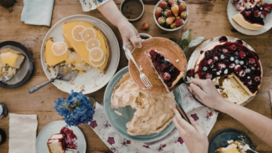 Tisch von oben mit unterschiedlichen Kuchen, Hände und Arme die sich etwas reichen
